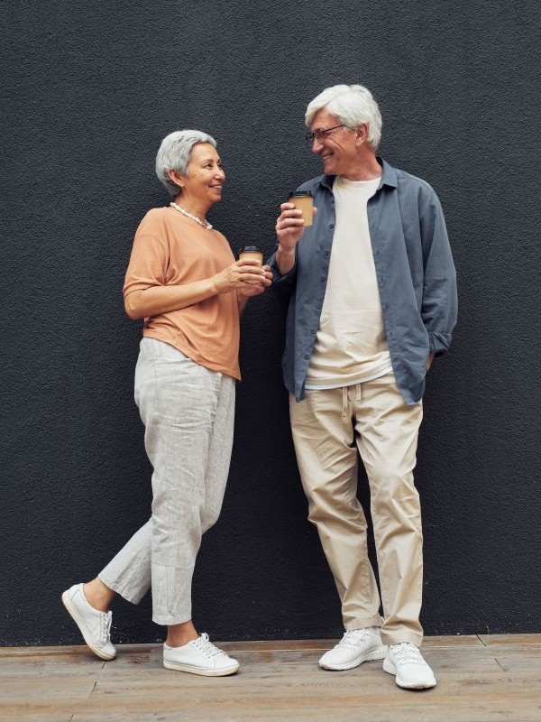 Two seniors standing in front of the black concrete wall facing each other with a cup in their hand.